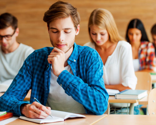 42896040 - focused on exam. group of concentrated young students writing something in their note pads while sitting at their desks in the classroom